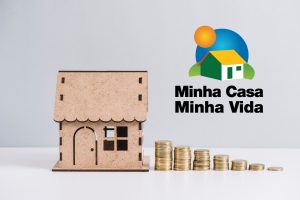 casa em miniatura ao lado de moedas e a logo do programa habitacional. Ilustrativa para Simulação Minha Casa Minha Vida.